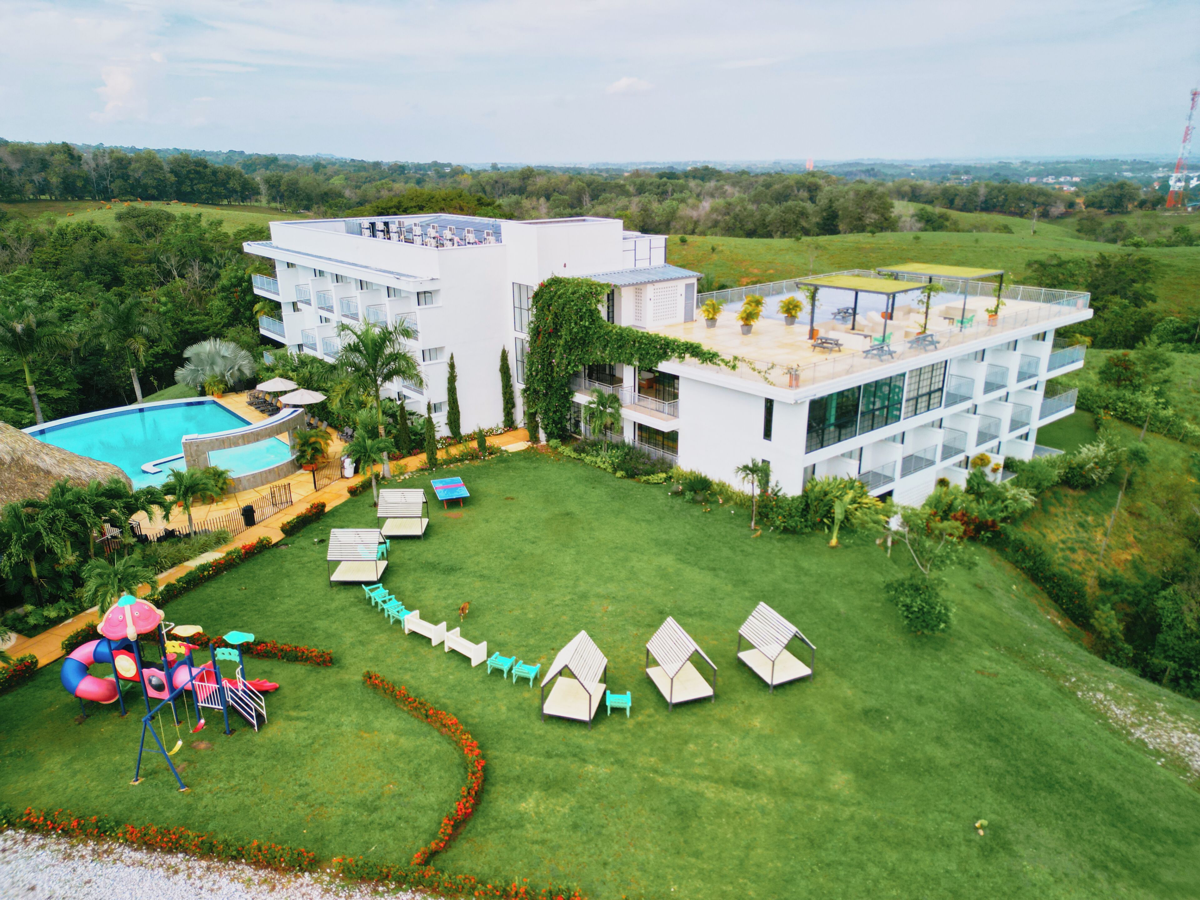 A modern hotel with a swimming pool, outdoor seating, and lush greenery.
