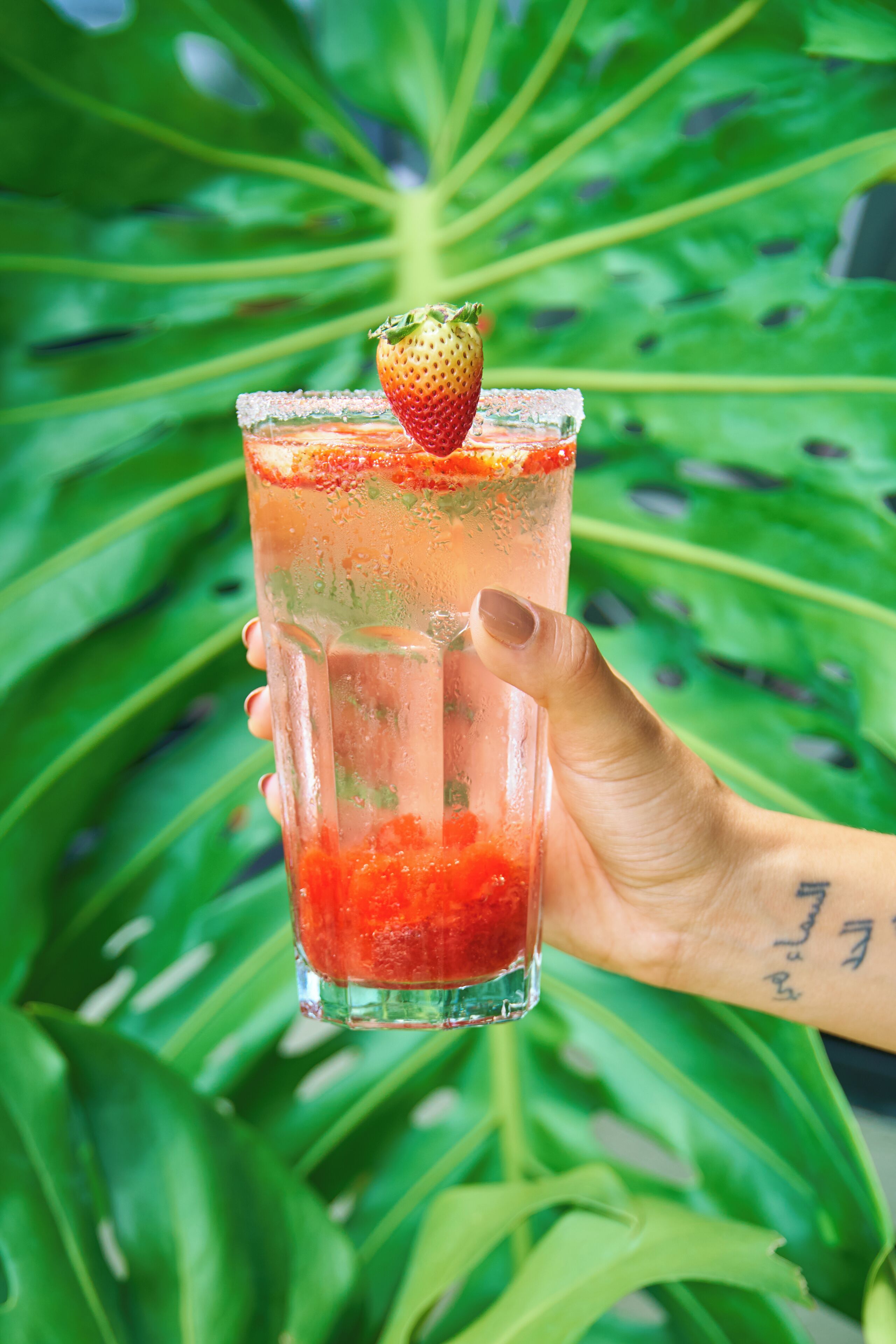 A hand holding a glass with a strawberry garnish.