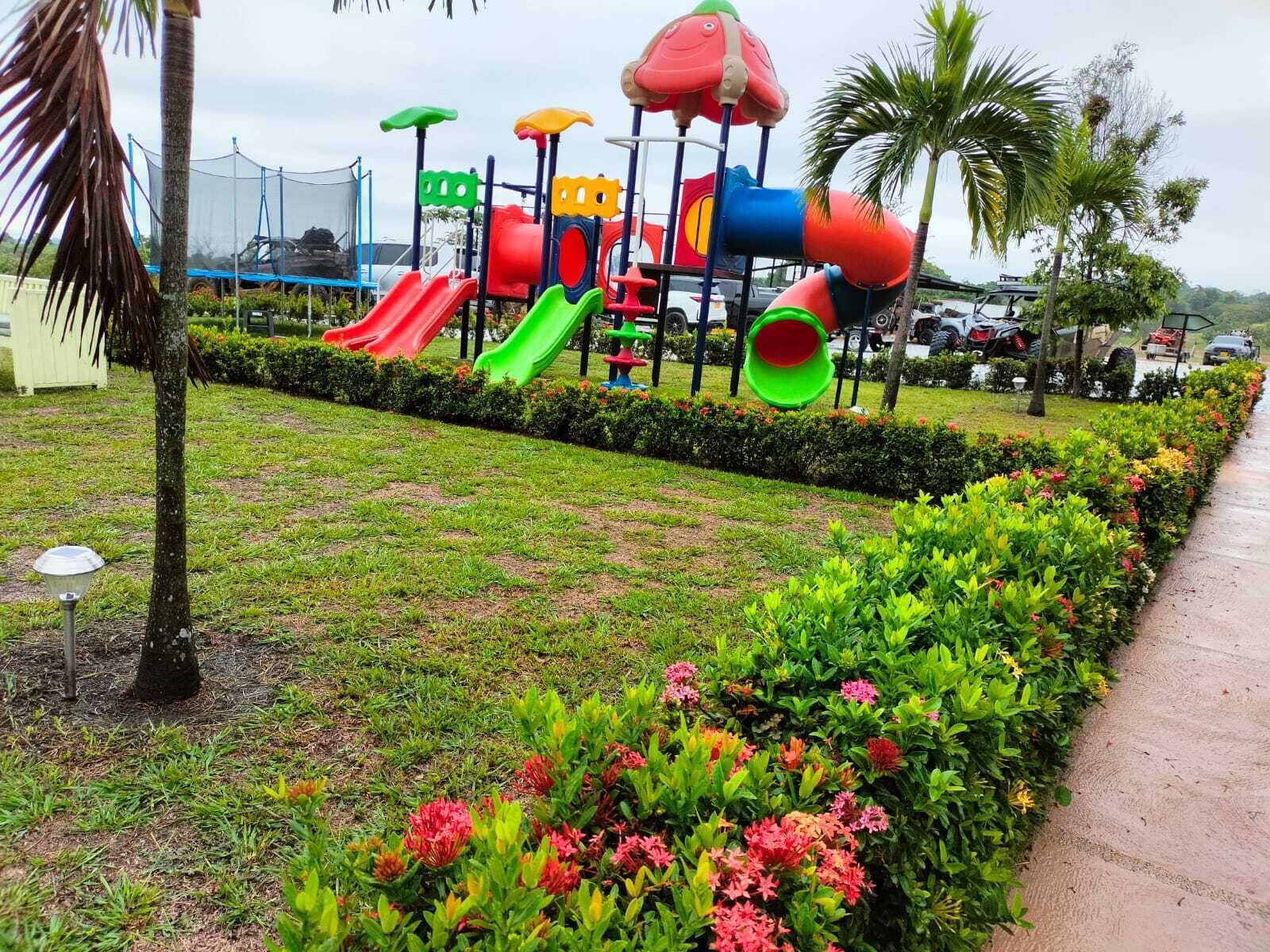 A playground with slides and climbing structures, surrounded by well-maintained hedges and flowering plants.