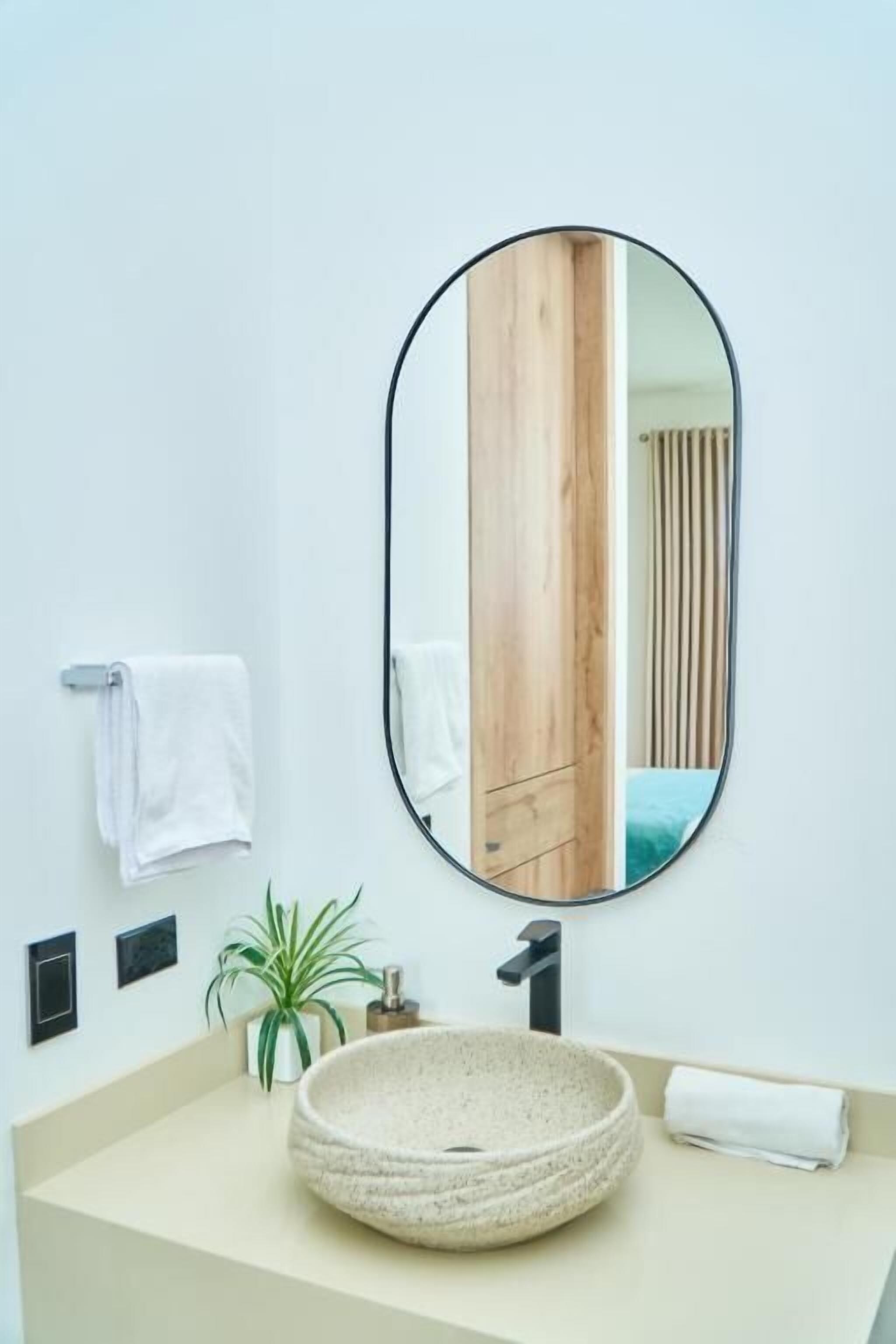 Un baño con un lavamanos tipo recipiente, un espejo, un perchero y una planta en maceta.