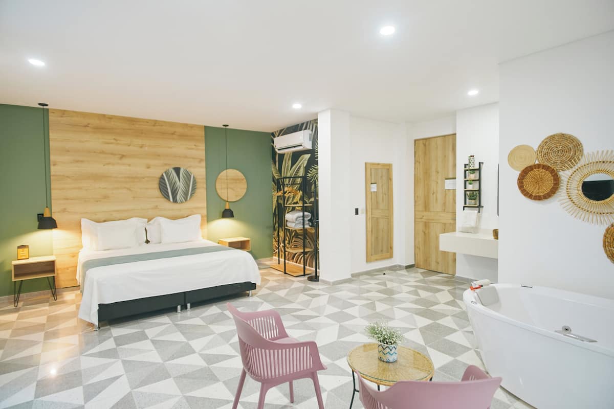 A modern hotel room with a bed, two chairs, a round table, a bathtub, and a shower area.