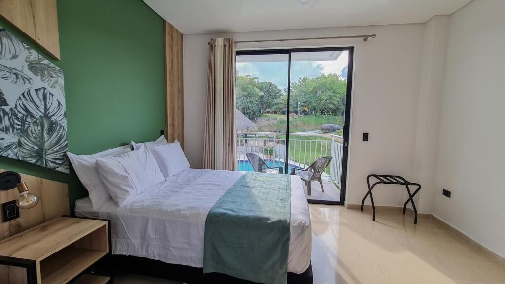 A hotel room with a bed, a nightstand, a chair, a balcony with a pool view, and a green wall.