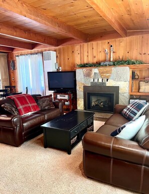 Ein gemütliches Wohnzimmer mit Holzwänden, einem Kamin aus Stein, Ledersofas, einem Flachbildfernseher und einem Kaminvorsatz.