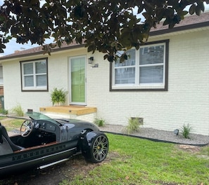 A house with a brick exterior, a green door, and a driveway with a vintage car parked in front.