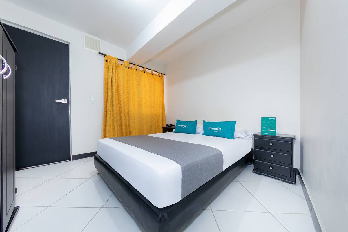 A hotel room with a bed, a nightstand, a desk, and a door.