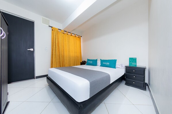 Quarto de hotel com cama, mesa de cabeceira, escrivaninha e porta.
