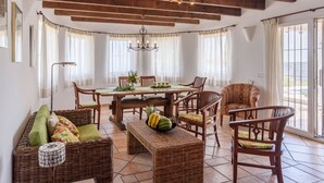 A dining area with a wooden table and chairs, surrounded by wicker furniture and a chandelier. - La Torre Cajiz by Ruralidays (Málaga)