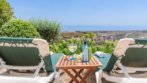 Two outdoor lounge chairs facing a scenic view of the sea, a small table with a glass of drink and a bottle, and a towel on the table. - La Torre Cajiz by Ruralidays (Málaga)