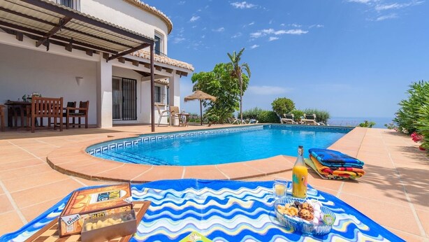 A poolside area with a tiled deck, a table with snacks, a bottle, and a chair. - La Torre Cajiz by Ruralidays (Málaga)