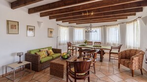 A spacious living area with a dining table, wicker furniture, and a chandelier. - La Torre Cajiz by Ruralidays (Málaga)
