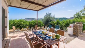An outdoor dining area with a table set for four, surrounded by chairs, with a view of a vineyard and hills in the background. - Las Ranas Cajiz by Ruralidays (Málaga)