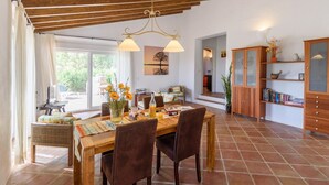 A dining area with a wooden table, chairs, and a chandelier. There is a bookshelf and a cabinet with glass doors. - Las Ranas Cajiz by Ruralidays (Málaga)