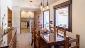A modern kitchen with wooden cabinets, a dining table with chairs, and a glass display case with food. - Cinco Soles Árchez by Ruralidays (Málaga)