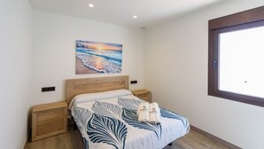 A bedroom with a bed, wooden headboard, bedside tables, a painting of a sunset, and a window with a view. - Cinco Soles Árchez by Ruralidays (Málaga)