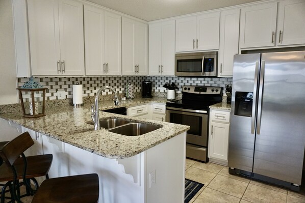 A modern kitchen with white cabinets, granite countertops, stainless steel appliances, and a bar area with stools.
