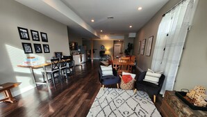 A spacious living room with a wooden floor, a large rug, and a dining area in the background. - Long Lake Oasis: To recharge or Work with a view (Lacey)