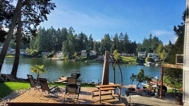 A lakeside deck with outdoor furniture, a swing, and a view of a lake and surrounding houses. - Long Lake Oasis: To recharge or Work with a view (Lacey)