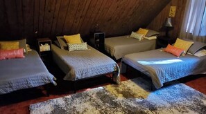 Three single beds with distinct headboards and pillows are arranged in this charming attic bedroom.