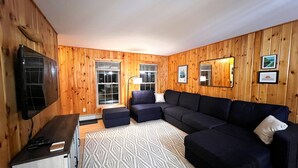 Una habitación con paneles de madera, un sofá modular, un televisor de pantalla plana y una alfombra estampada.