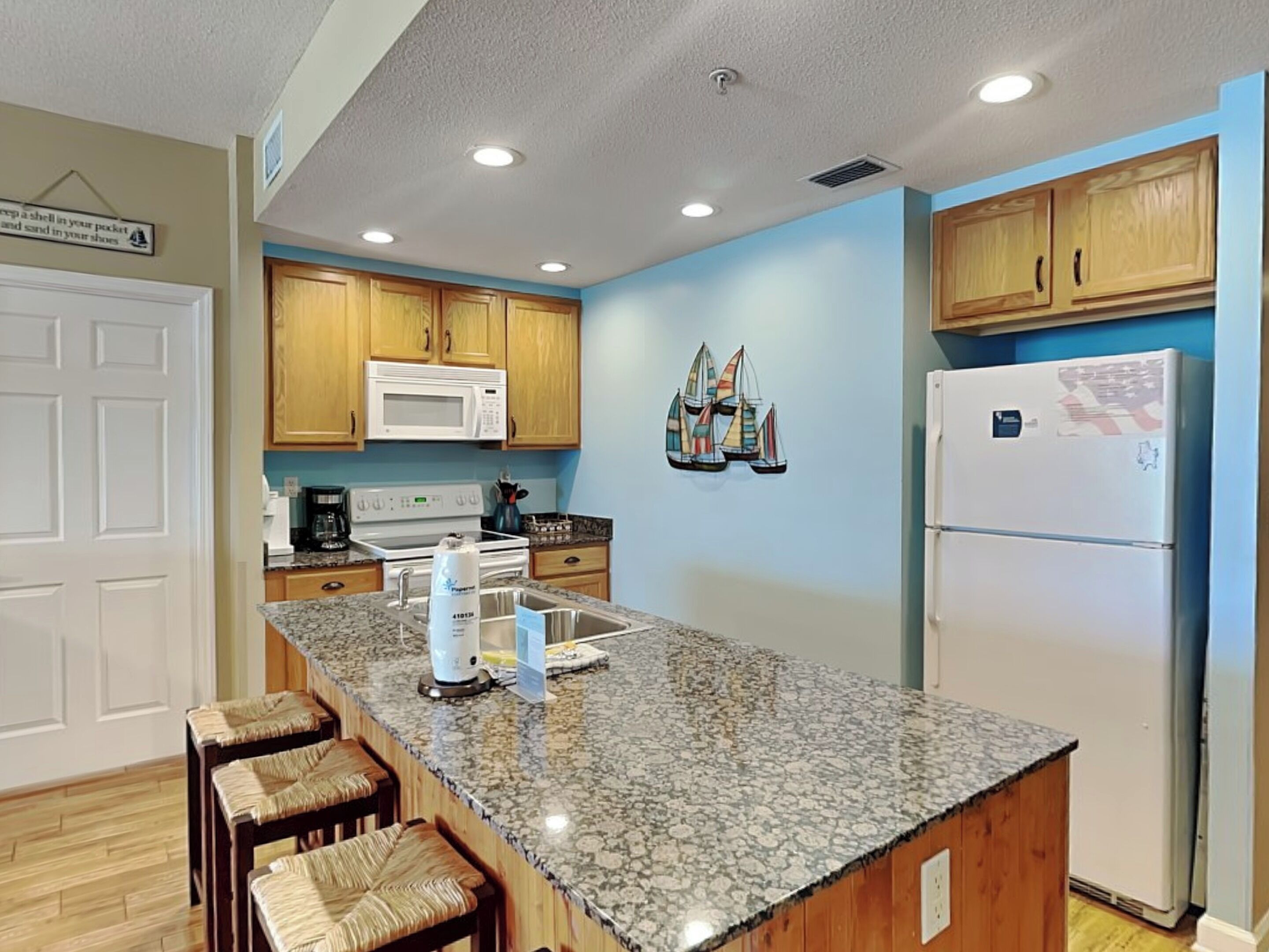 A kitchen with wooden cabinets, a granite countertop, a microwave, a stove, and a refrigerator.