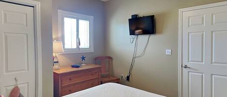 A bedroom with a bed, a dresser, a television mounted on the wall, and a ceiling fan.