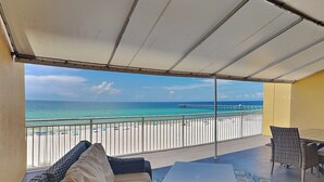 Un balcón con vista a la playa y al muelle, amueblado con un sofá, una mesa y sillas.