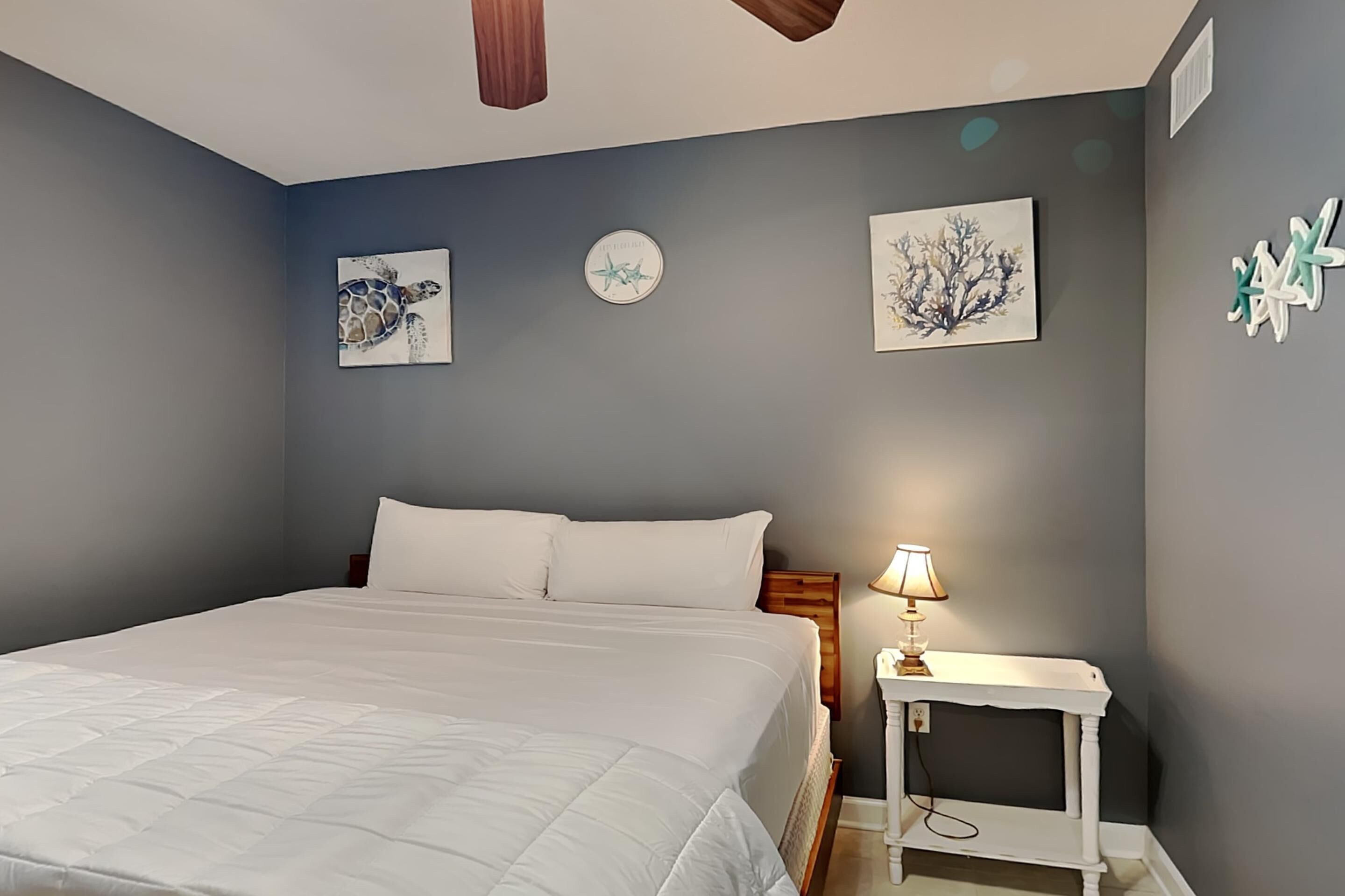 A bedroom with a large bed, a bedside table with a lamp, and wall art including a turtle and a starfish.