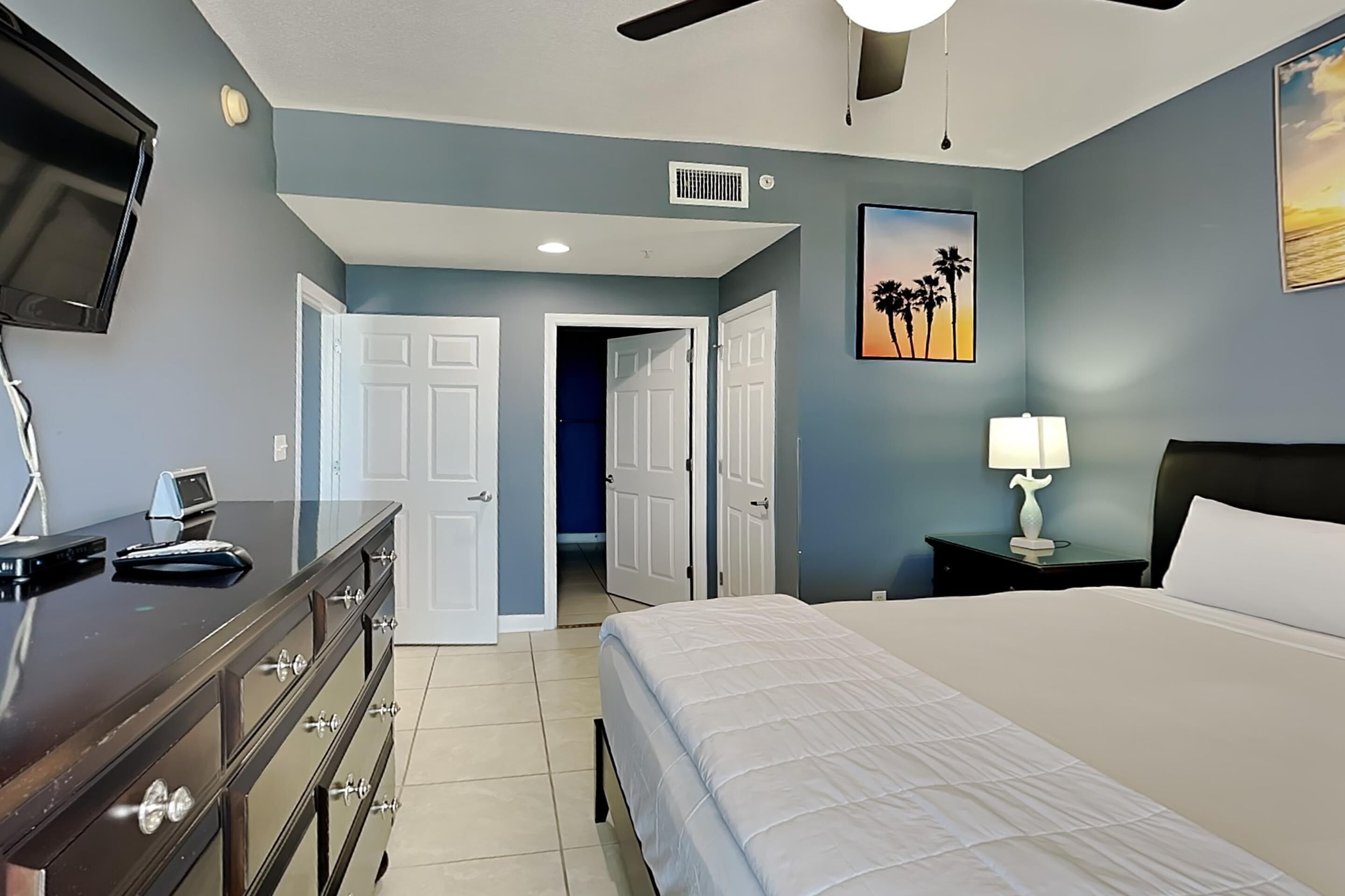 A bedroom with a bed, dresser, TV, and artwork.