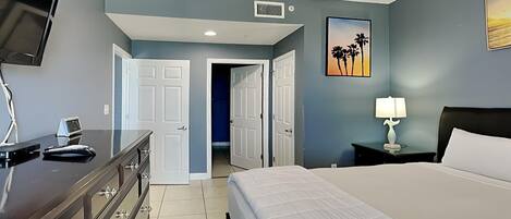 A bedroom with a bed, dresser, TV, and artwork.