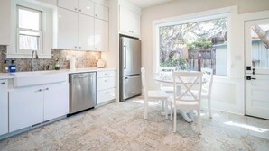 Een moderne keuken met witte kasten, roestvrijstalen apparatuur en een eethoek met witte stoelen.