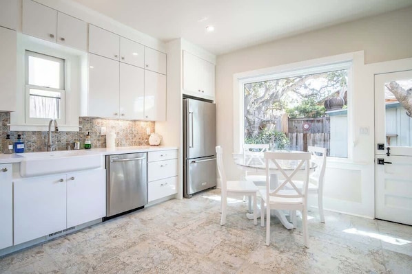 Een moderne keuken met witte kasten, roestvrijstalen apparatuur en een eethoek met witte stoelen.