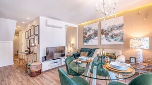 A modern living room with a dining area, featuring a glass table, green chairs, a flat-screen TV, and artwork on the walls. - GuestReady - Whole apartment in Lisbon (Lisboa)