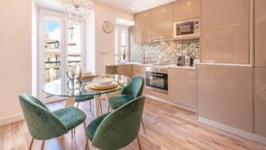 A modern kitchen with a glass dining table, green chairs, and a chandelier. - GuestReady - Whole apartment in Lisbon (Lisboa)