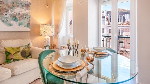 A modern dining area with a glass table, white plates, and candles. A sofa and a painting are visible in the background. - GuestReady - Whole apartment in Lisbon (Lisboa)