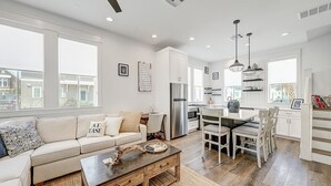 A modern kitchen with white cabinets, stainless steel appliances, and a dining area with white chairs. - Bright, modern home with shaded porch, AC & on-site golf, pool, beach access (Port Aransas)