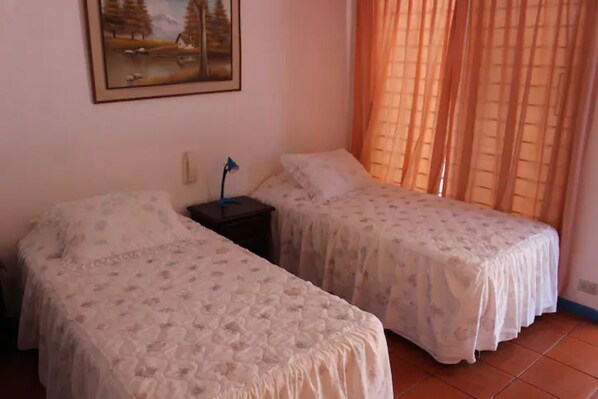 Une chambre avec deux lits, une table de chevet, une lampe et un tableau au mur.