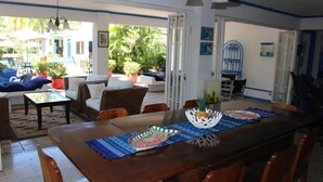 A dining area with a wooden table, blue placemats, and chairs. There is a view of an outdoor seating area with umbrellas and potted plants.