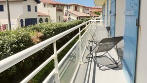 A balcony with a metal railing, a chair, and a building with blue doors in the background. - HOSSEGOR. Central beach. Flat for 4 persons. Free Wifi. (SOORTS HOSSEGOR)