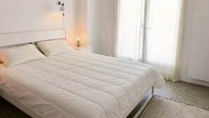 A neatly made bed in a room with a large window, a bedside lamp, and a plain wall. - HOSSEGOR. Central beach. Flat for 4 persons. Free Wifi. (SOORTS HOSSEGOR)
