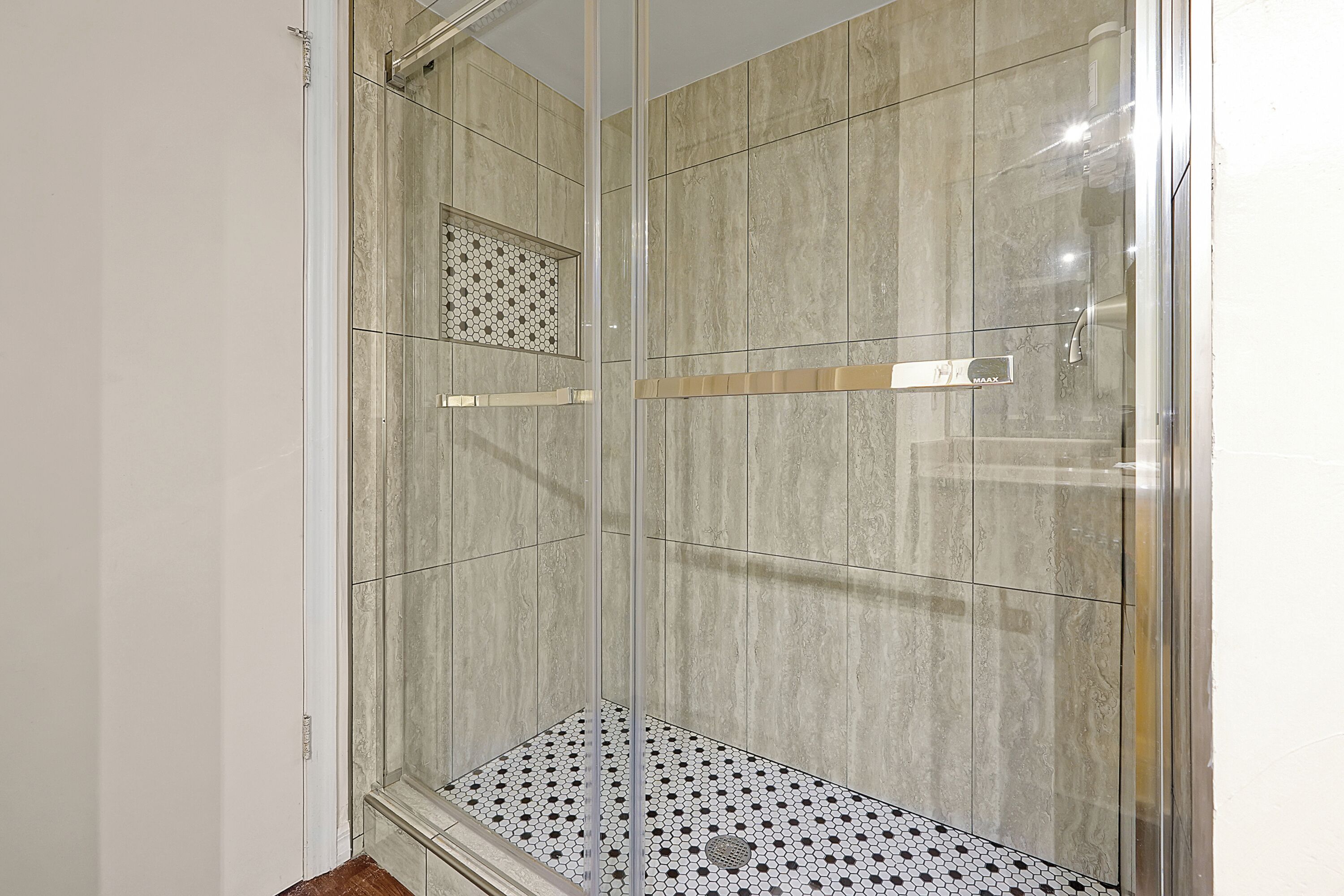 Una ducha con cerramiento de vidrio, piso y paredes de azulejos.