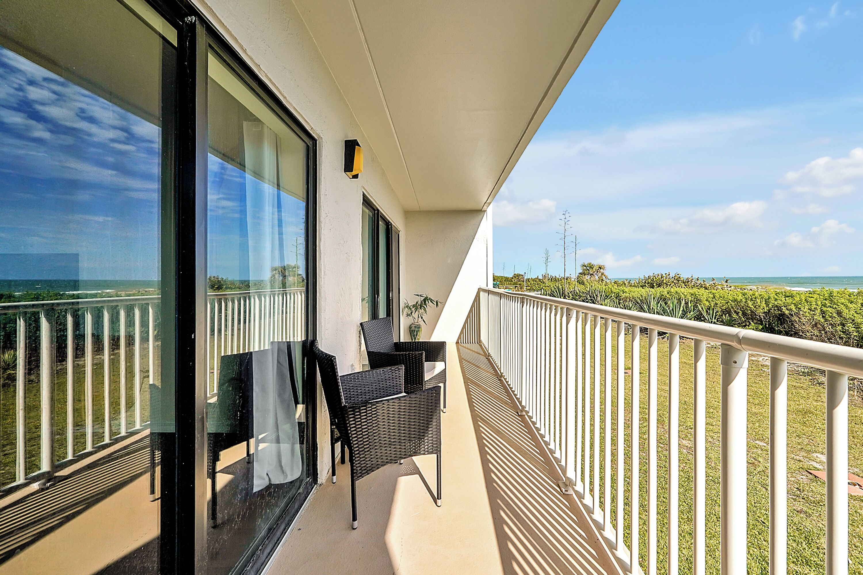 A balcony with a view of the sea, a table with chairs, and a railing.