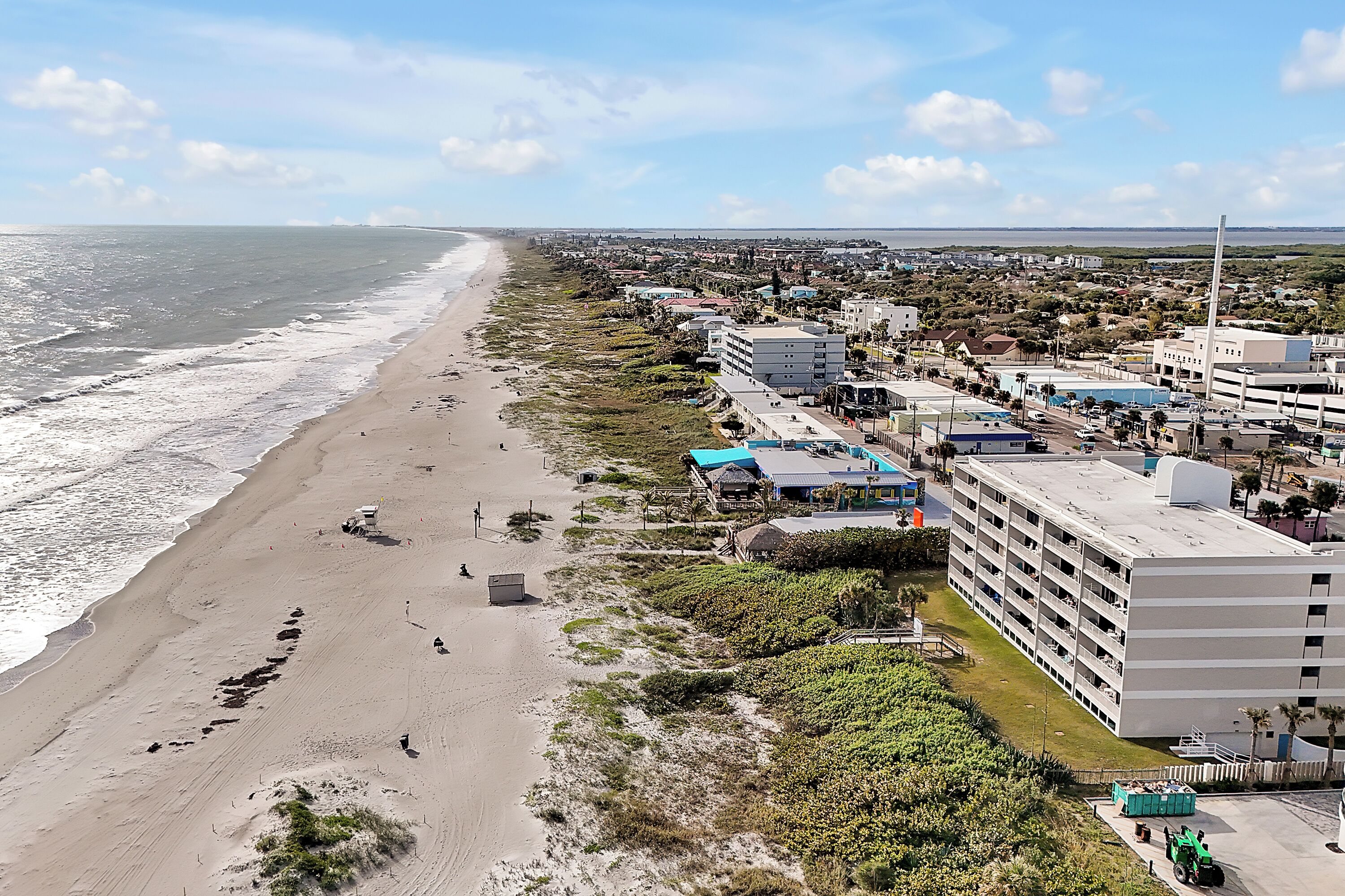 A coastal hotel with a beach view, multiple floors, and a parking area.