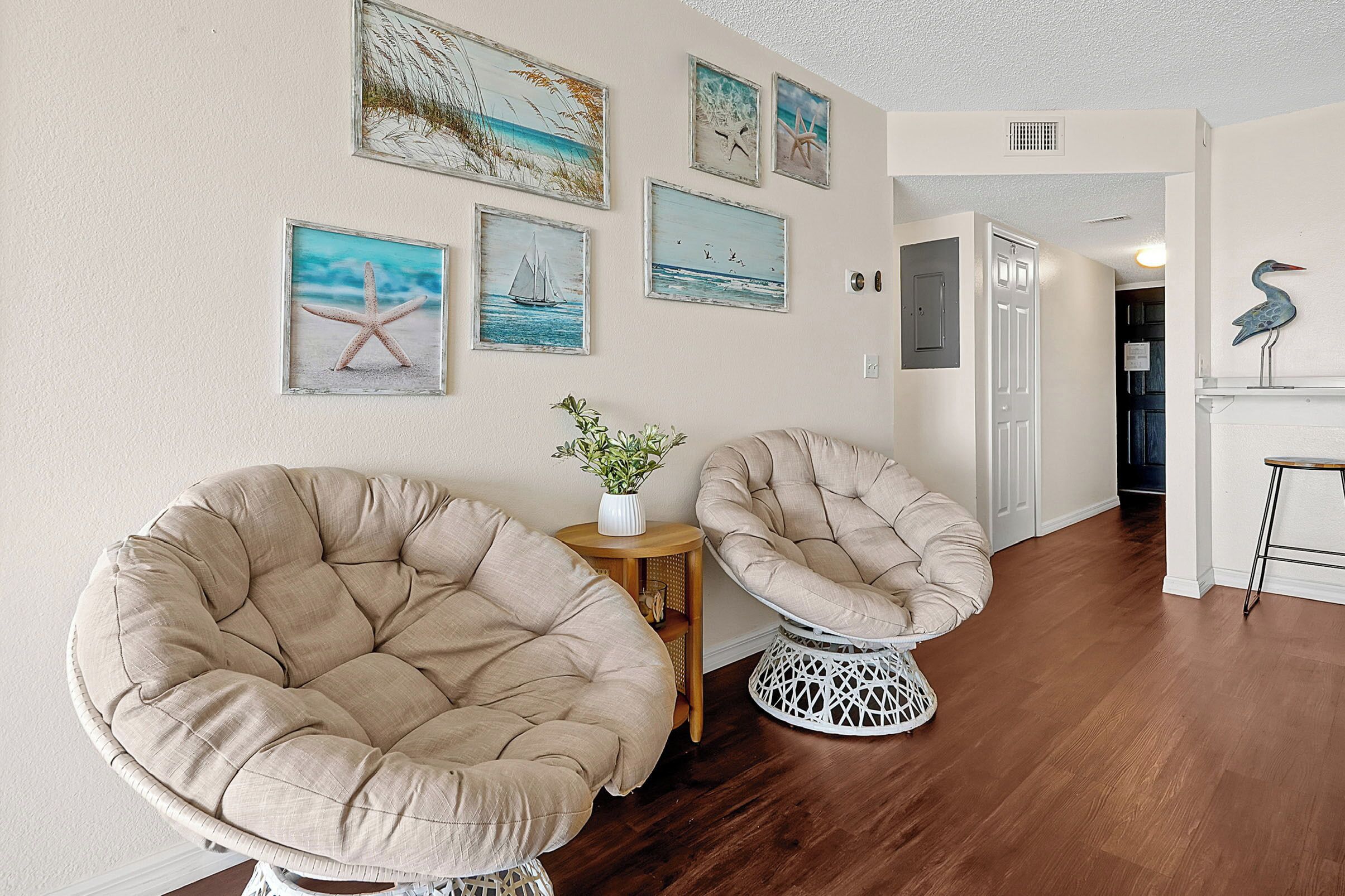 A room with two large, beige, tufted chairs, a small wooden side table with a plant, and a white, intricately designed stool.