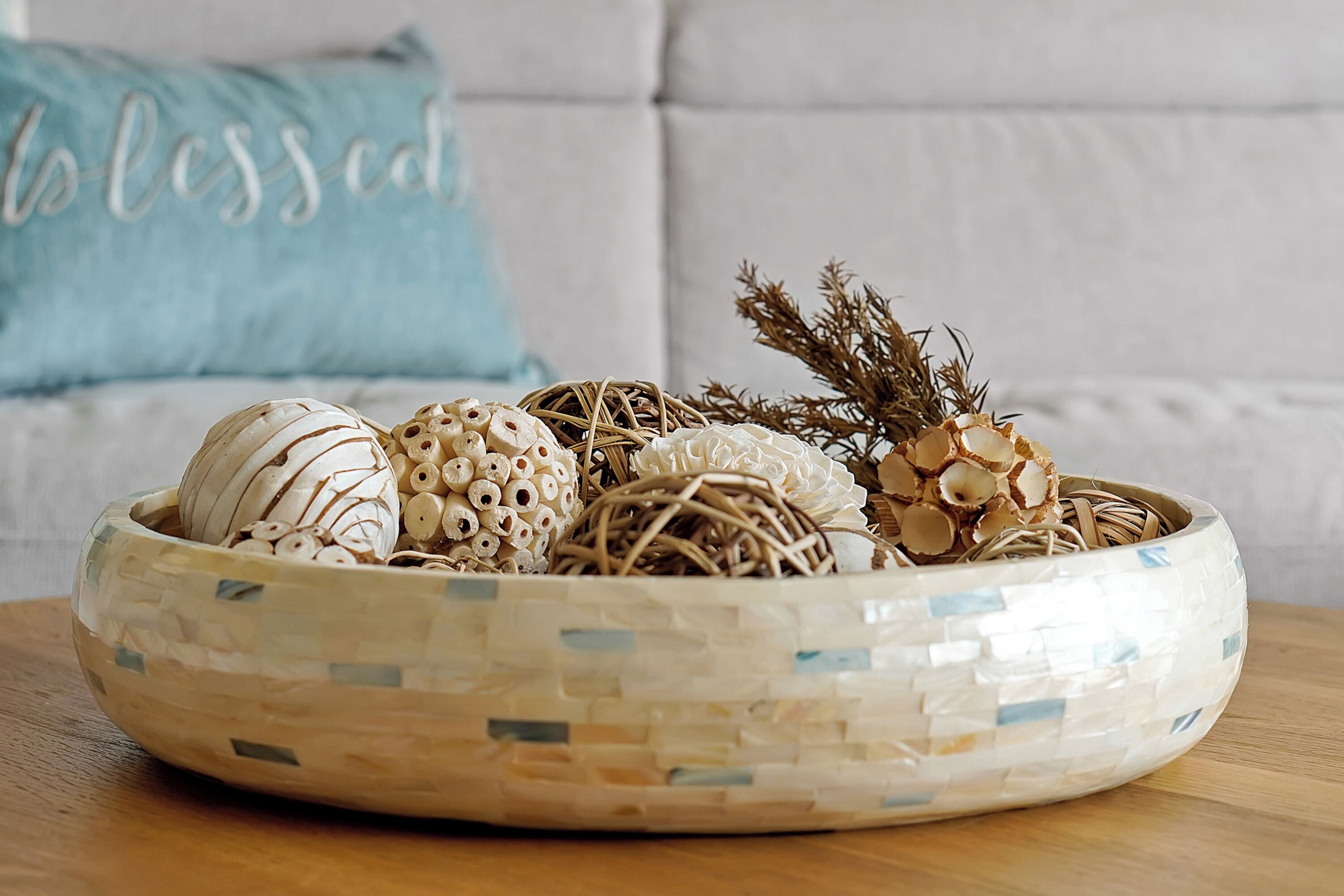 Un cuenco decorativo con varios adornos sobre una mesa de madera, frente a un sofá con un cojín.