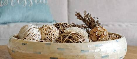 Un cuenco decorativo con varios adornos sobre una mesa de madera, frente a un sofá con un cojín.