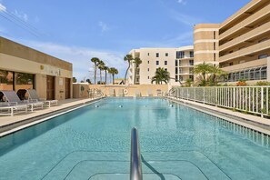 Une piscine avec des chaises longues et, au fond, un bâtiment doté de nombreux balcons.