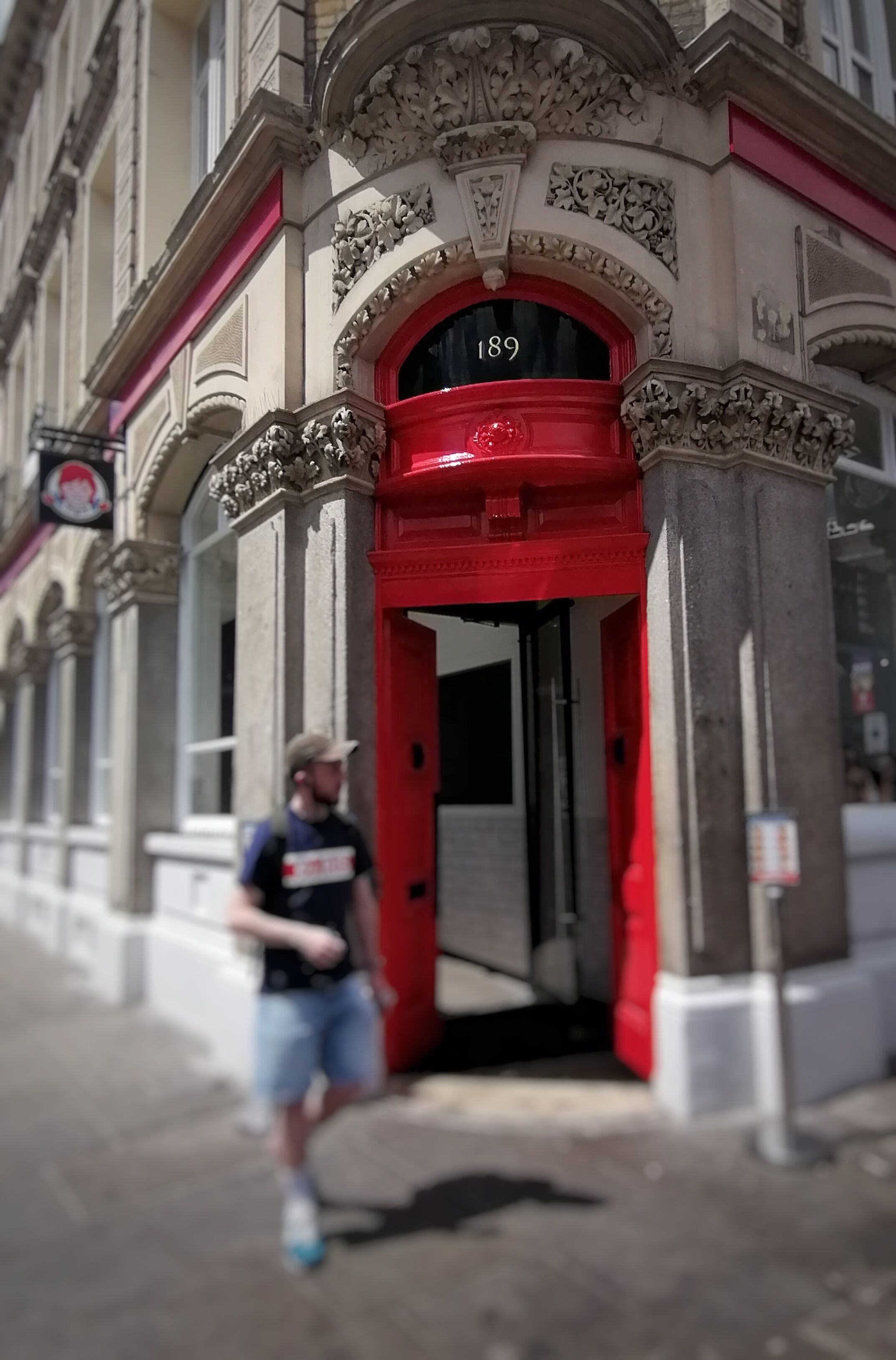 A building with ornate architectural details, a red entrance, and the number 189 on the door.