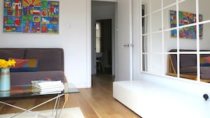 Un salon moderne avec un canapé, une table basse et une bibliothèque. Les murs sont ornés de peintures abstraites aux couleurs vives.
