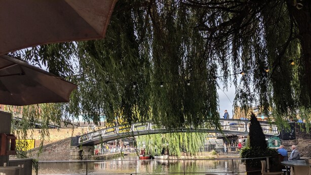 Un espace extérieur aménagé avec des tables et des chaises, offrant une vue sur un plan d’eau et un pont.