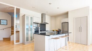 A modern kitchen with a central island, bar stools, a stainless steel range hood, and a built-in oven. - Hekerua Bay Retreat - Coastal Views (Waiheke Island)